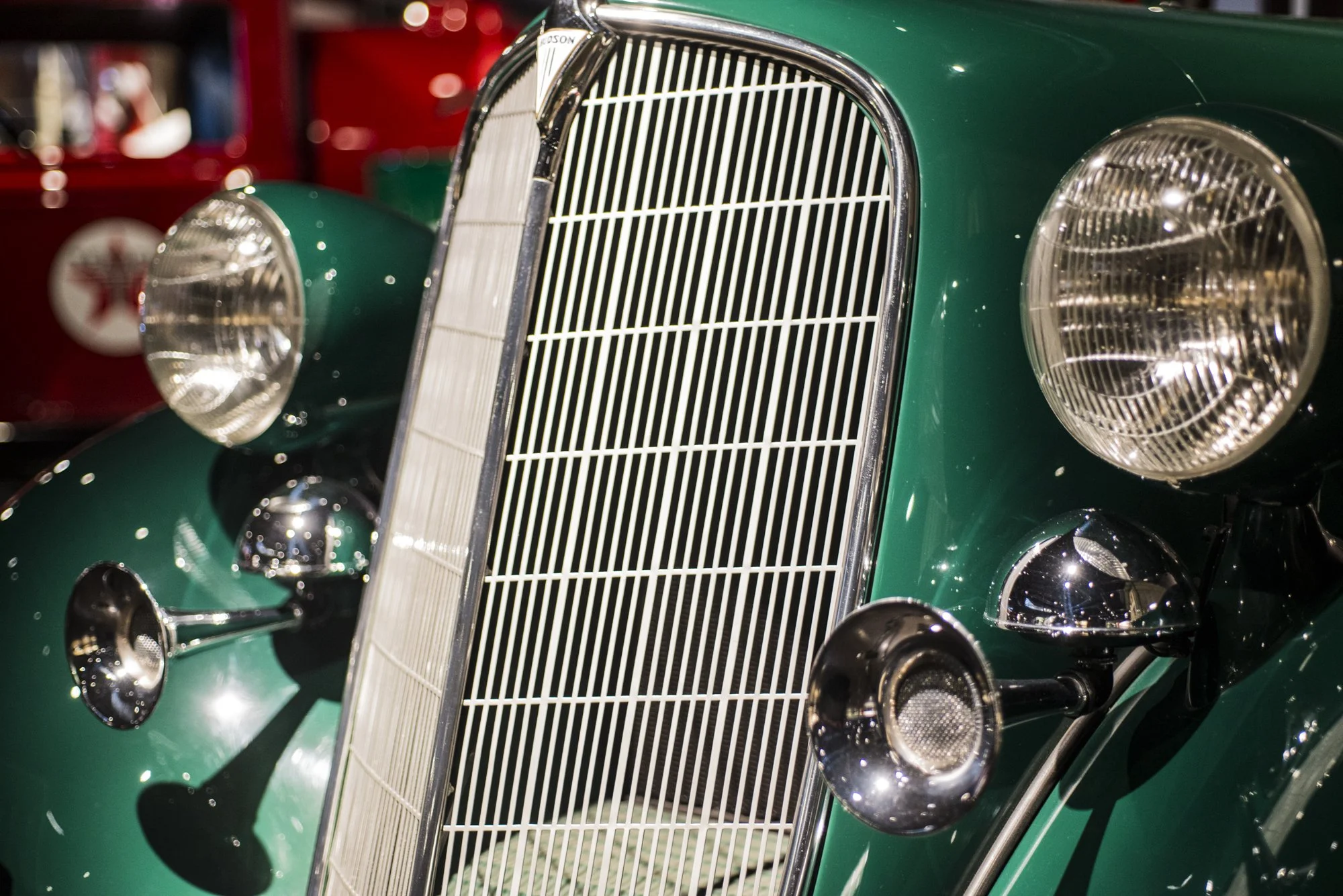Close-up of a vintage green car's front grille, headlights, and bumper in a museum setting.