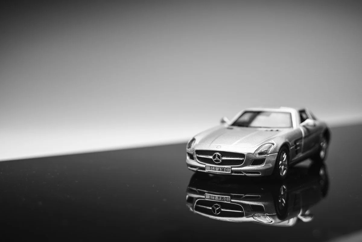 A black and white photo of a miniature Mercedes-Benz car model on a reflective surface.