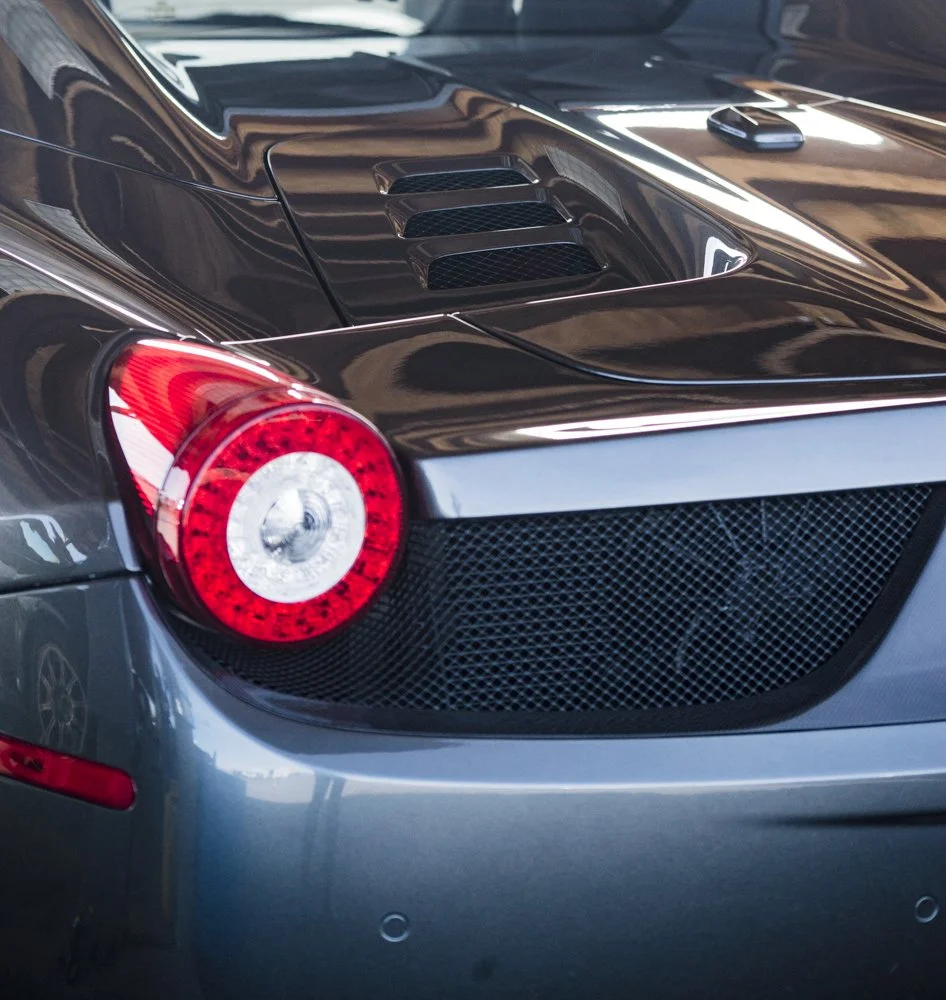 Close-up of the back of a black sports car, showing the taillight, rear grille, and rear engine vents.