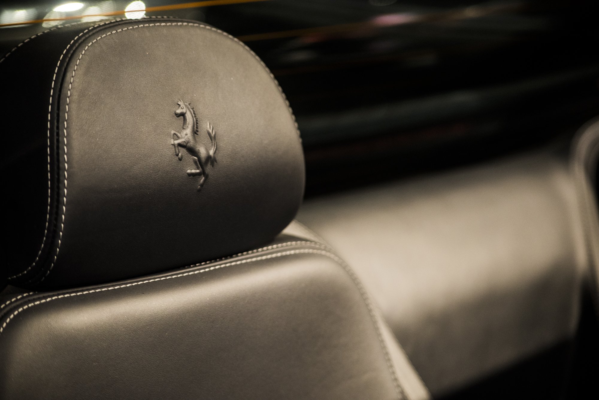 Close-up of a car's headrest with the Ferrari logo embossed on it, made of black leather with white stitching.