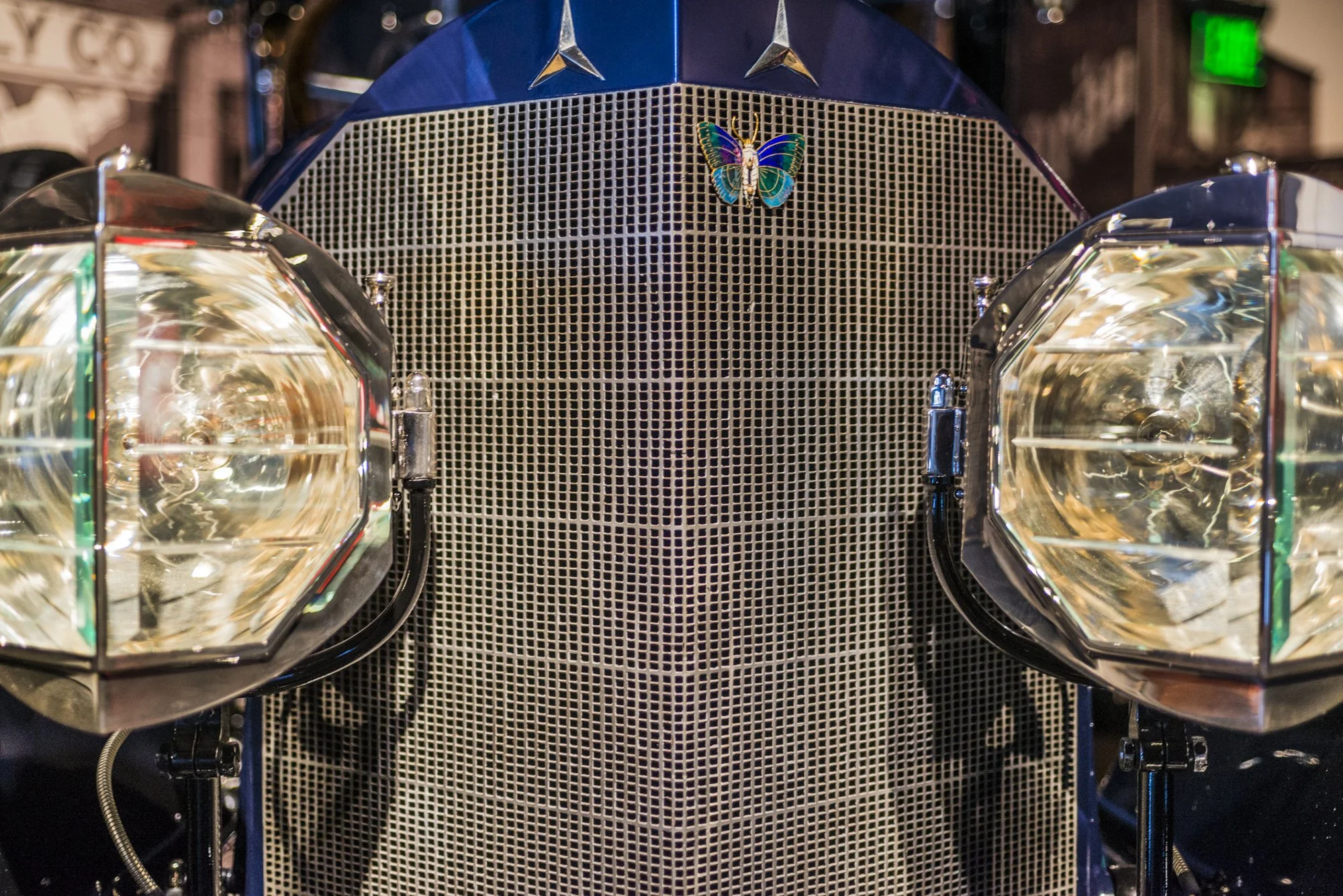 Close-up of a vintage Mercedes-Benz car front grille with a colorful butterfly sticker on it, and two large fog lights flanking the grille.