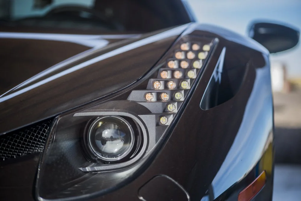 Close-up of a sleek black sports car's front headlight and LED daytime running lights.