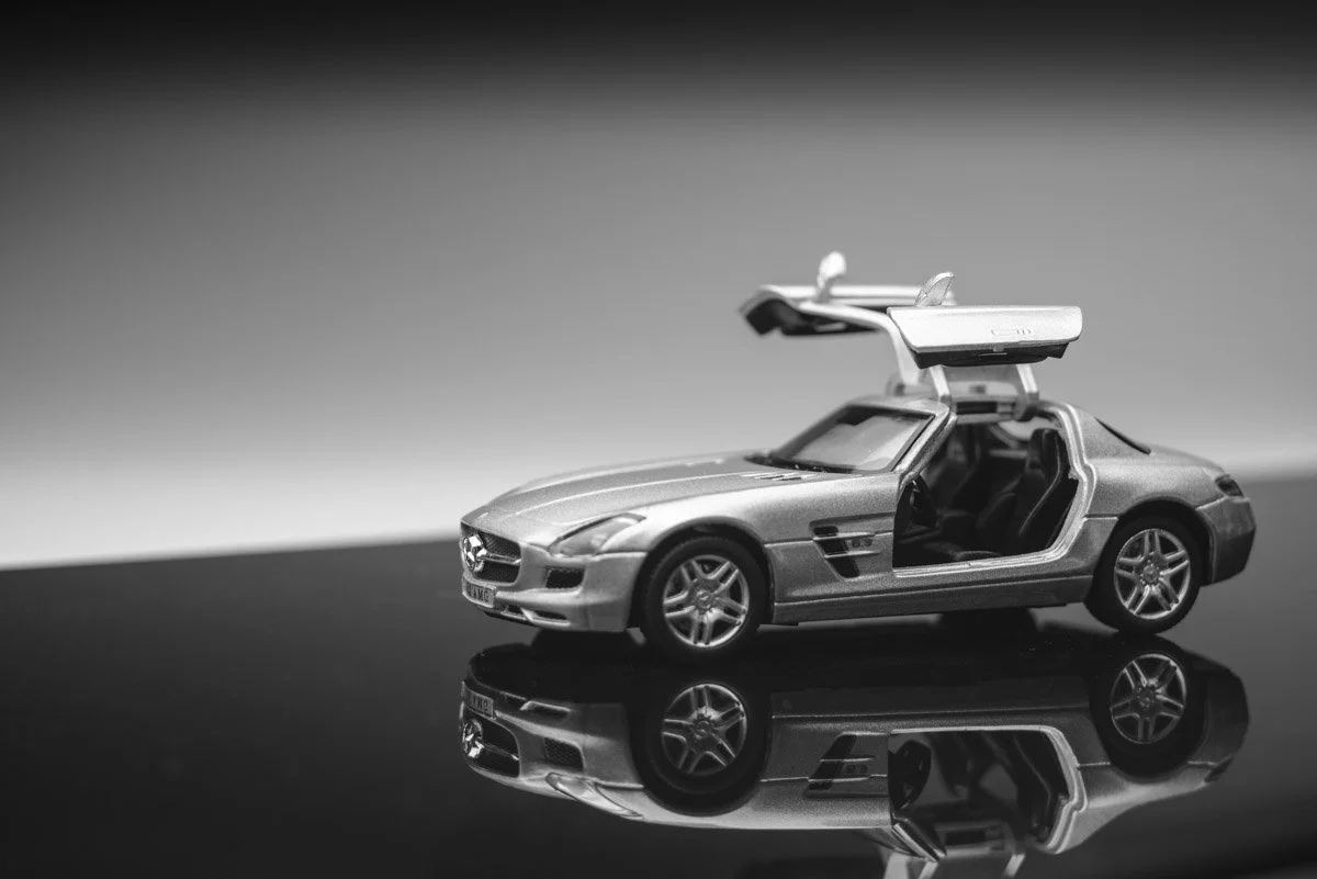 A black and white photo of a detailed model of a sports car with gull-wing doors open, placed on a reflective surface.