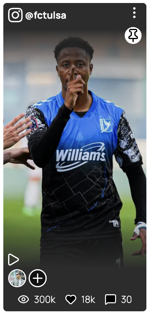 A soccer player in a blue and black jersey, making a shushing gesture with his finger to his lips during a game.