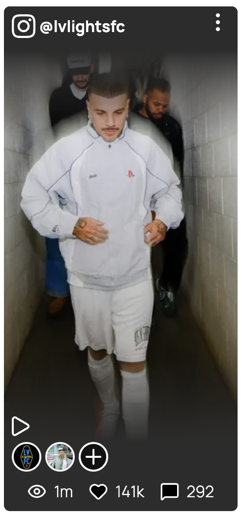 A young man walking down a narrow hallway with gray brick walls, dressed in a white tracksuit with a PlayStation logo, white shorts, and white knee-high socks, with two men following behind him.
