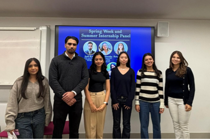 Group of six students standing in front of a digital presentation at a seminar titled 'Spring Week and Summer Internship Panel.'