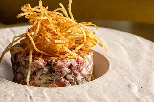 A serving of beef tartare topped with crispy fried onion strings on a white plate.