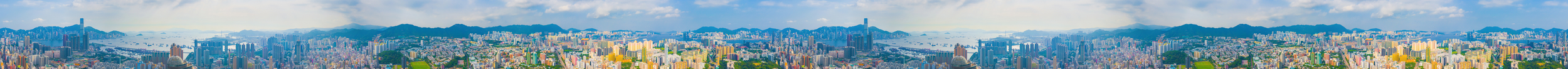 Panoramic view of a city skyline with numerous tall buildings, green hills in the background, and a partly cloudy sky.