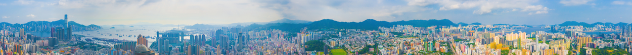 A panoramic cityscape of Hong Kong with a harbor, numerous high-rise buildings, and mountains in the background.