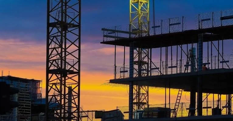 Construction site with steel framework and cranes during sunset with colorful sky.