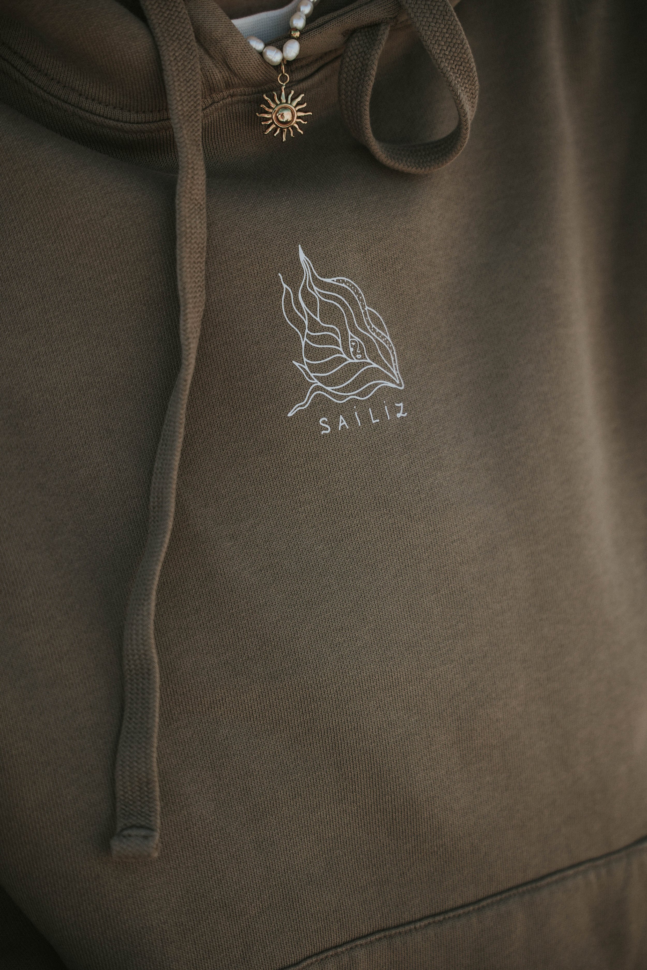Hoodie marron avec un logo en blanc et le mot 'SAILIZ' en dessous, porté par une personne avec un collier en perles et un pendentif en forme de soleil, pour les femmes navigatrices