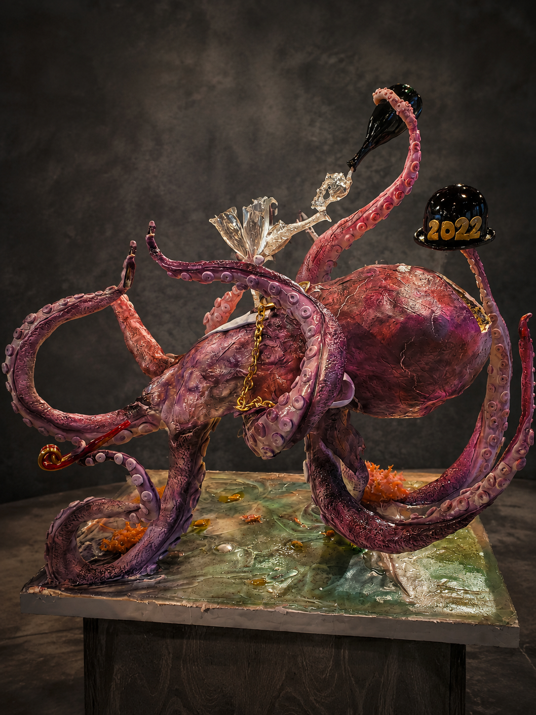 Cake sculpture of an octopus with extended tentacles, displaying the year 2022 on a black hat, set on a textured base. From the show Holiday Wars Championship.