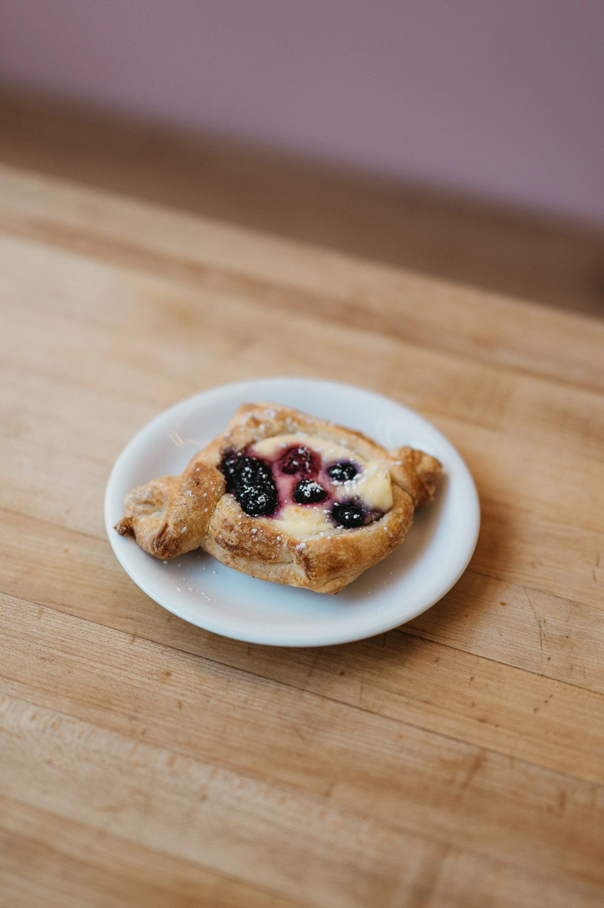 A blueberry Danish pastry on a small white plate set on a wooden table.