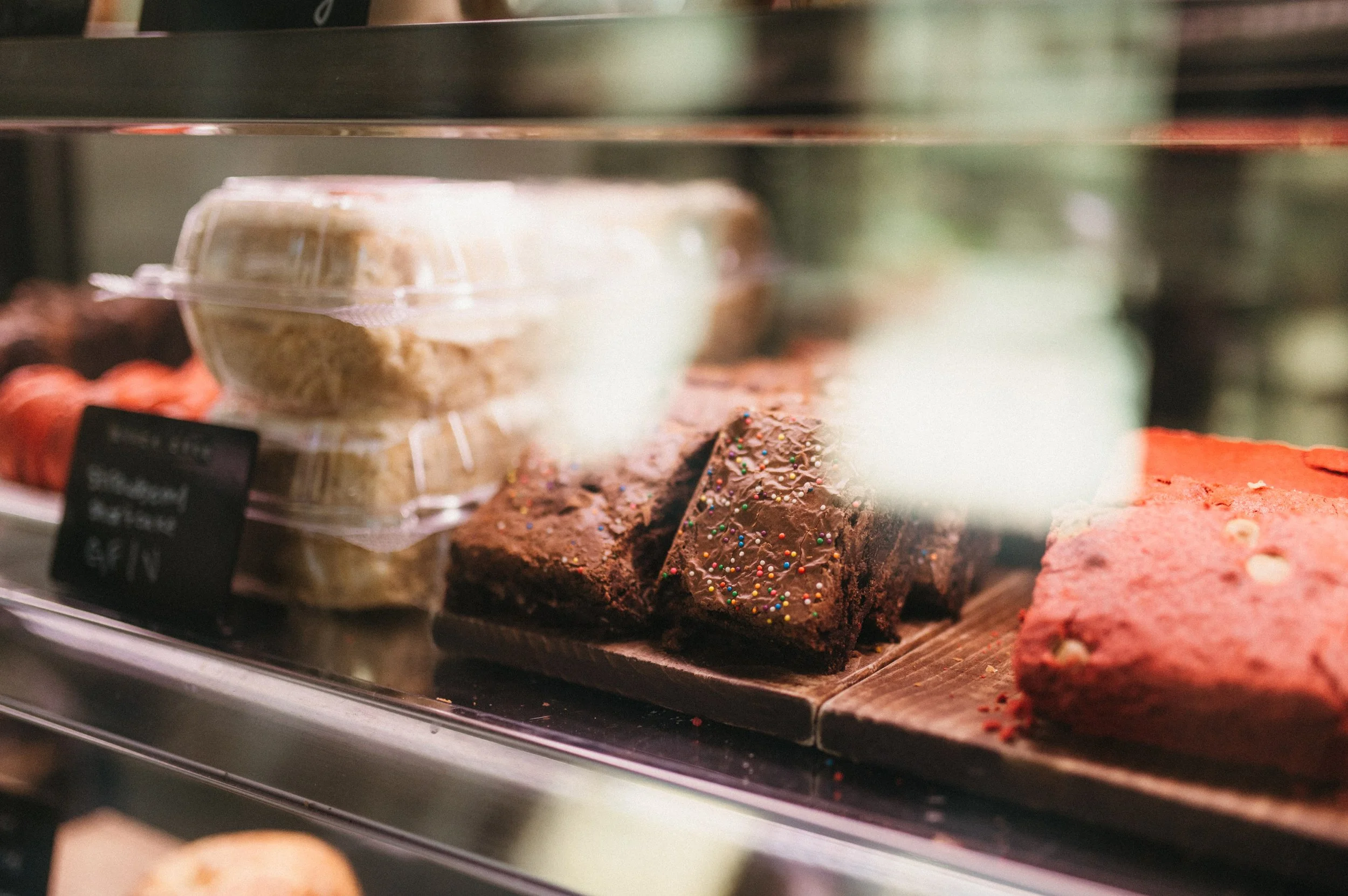 Assorted bakery items including chocolate cake with colorful sprinkles and a pink cake in display case.