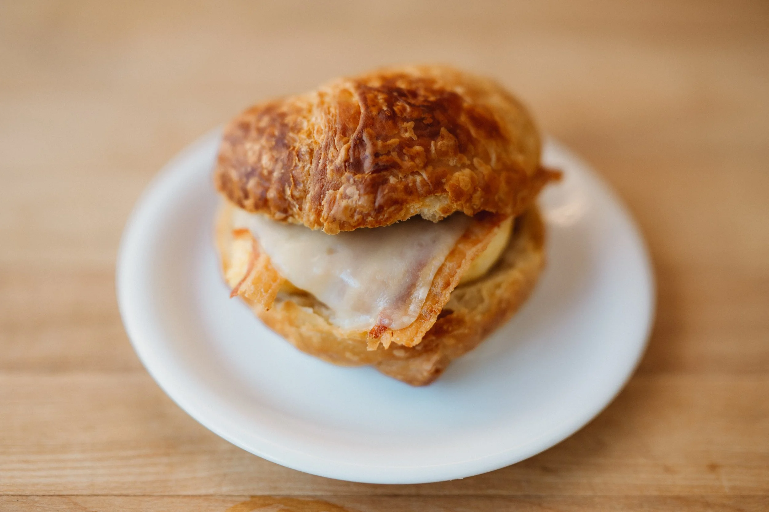 A croissant sandwich filled with cheese, ham, and fried egg on a white dish.