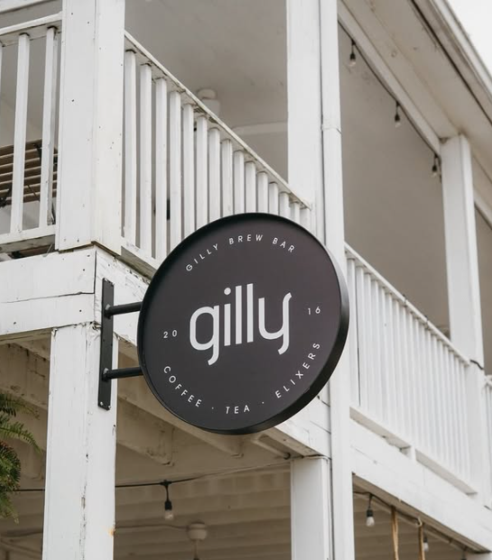 Round black sign on a white building that reads "Gilly" with additional text "GILLY BREW BAR Coffee Tea Elixers" and "2016".