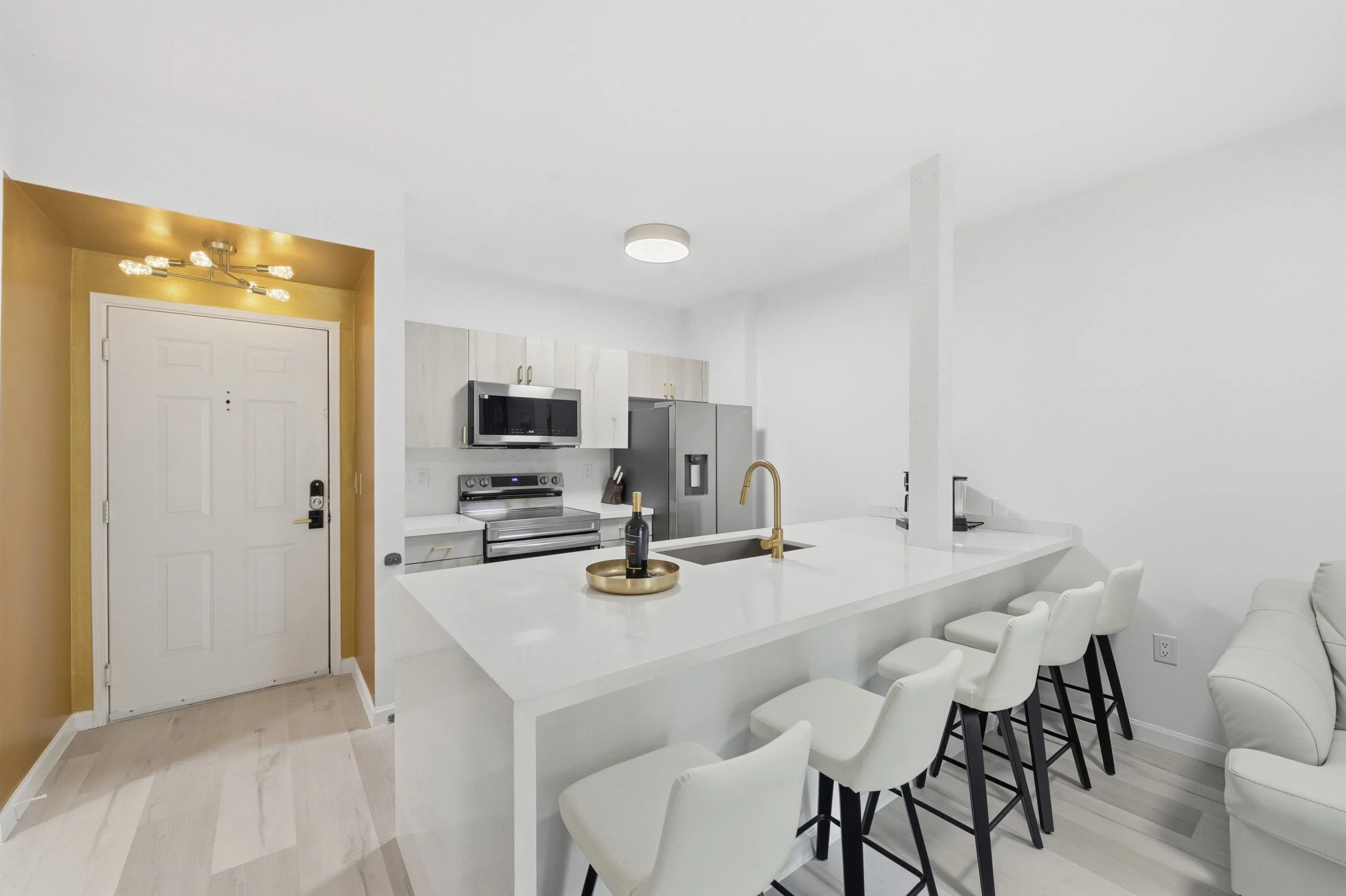 Open white kitchen and entry area with a gold faucet and counter seating.