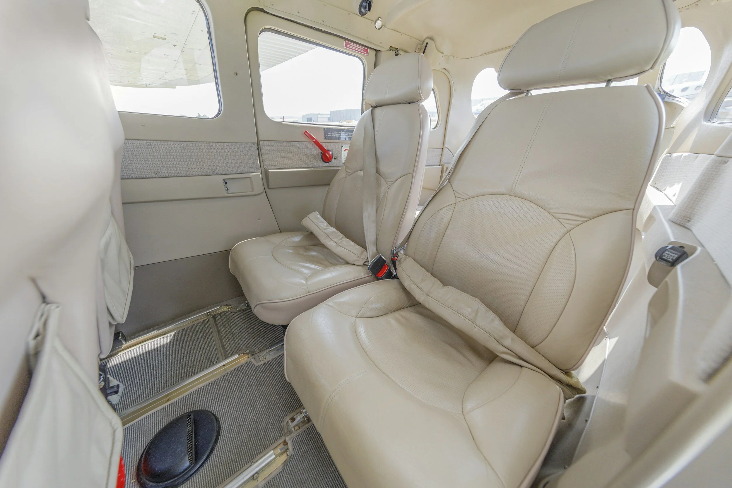 Interior of a small aircraft with cream-colored leather seats and windows showing the tarmac outside.