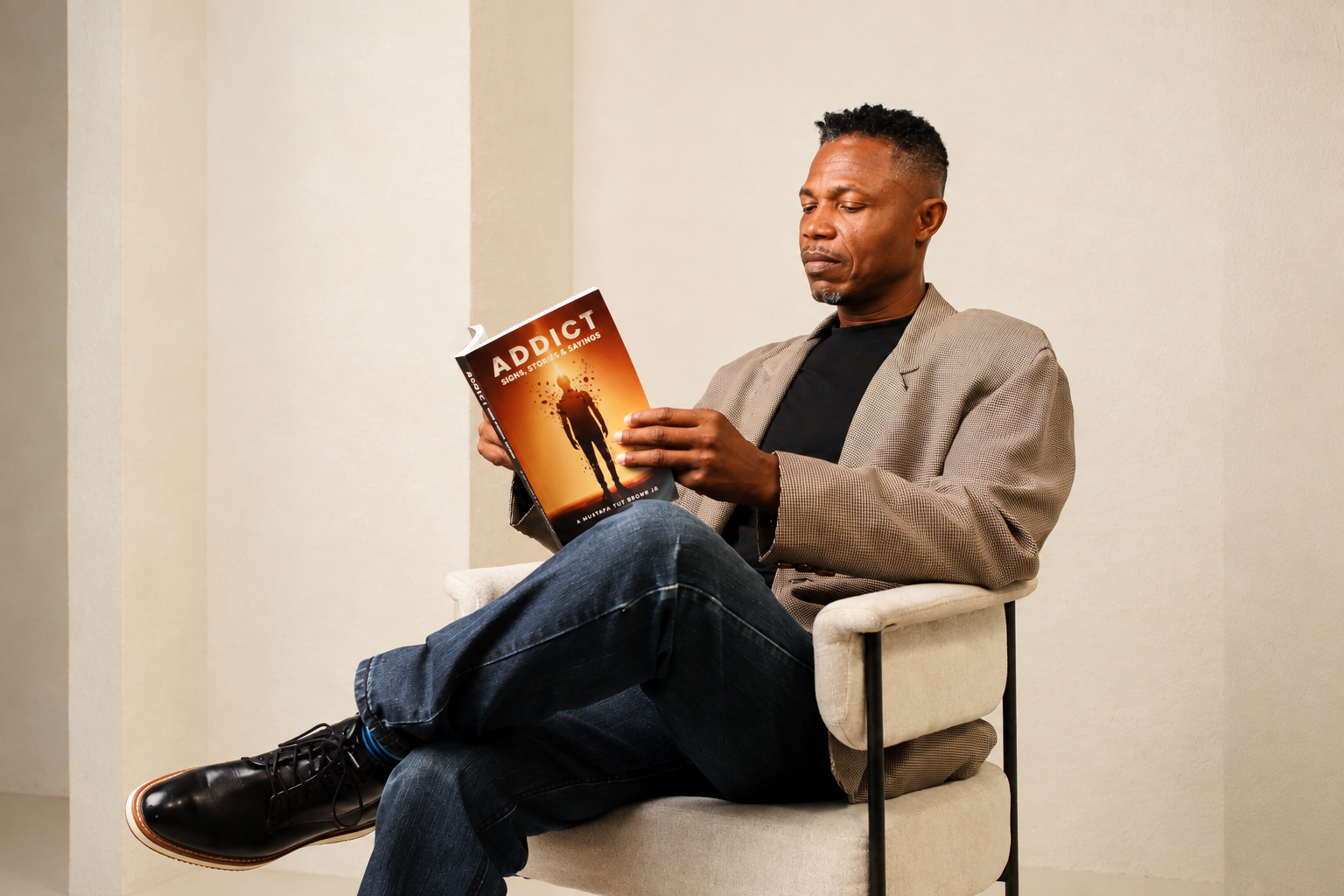 A. Mustafa Tut Brown Jr. seated and reading his book ADDICT: Signs, Stories & Sayings.