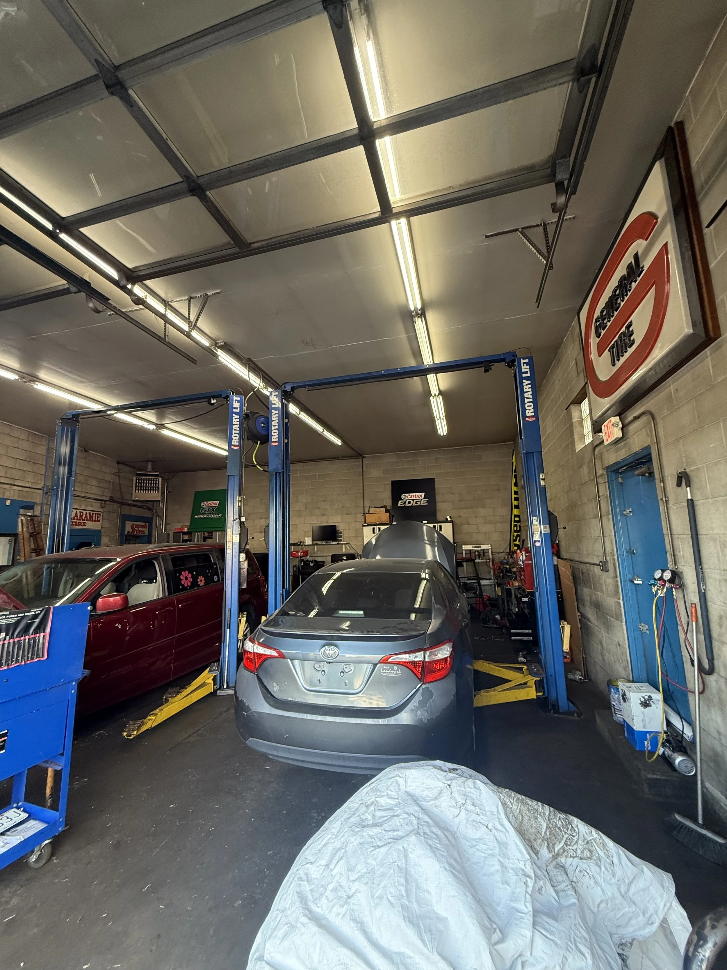 Inside a garage with two cars on a car lift, tools, and equipment around.