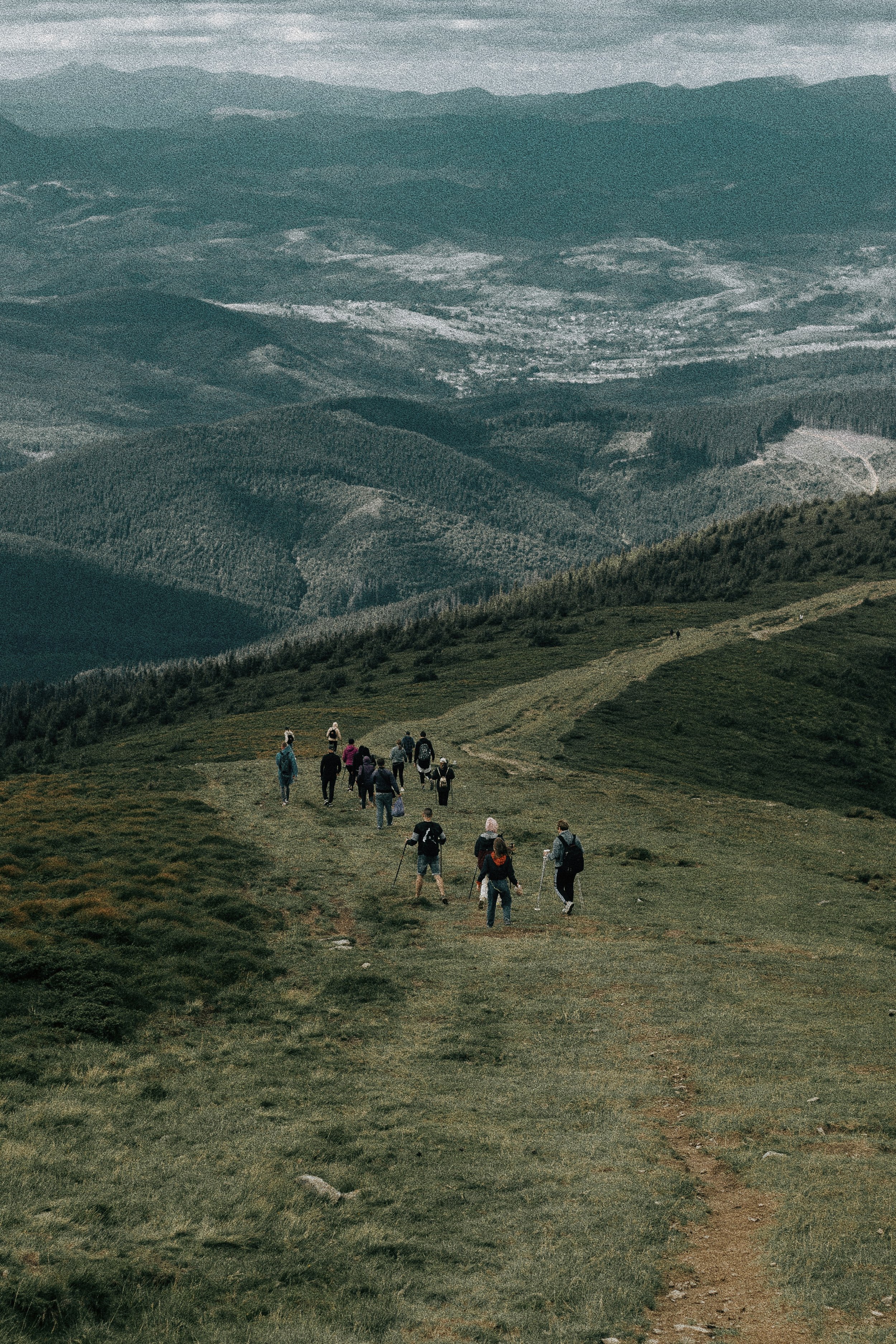 A group of hikers walking along a trail in a mountainous area with forested hills in the background.