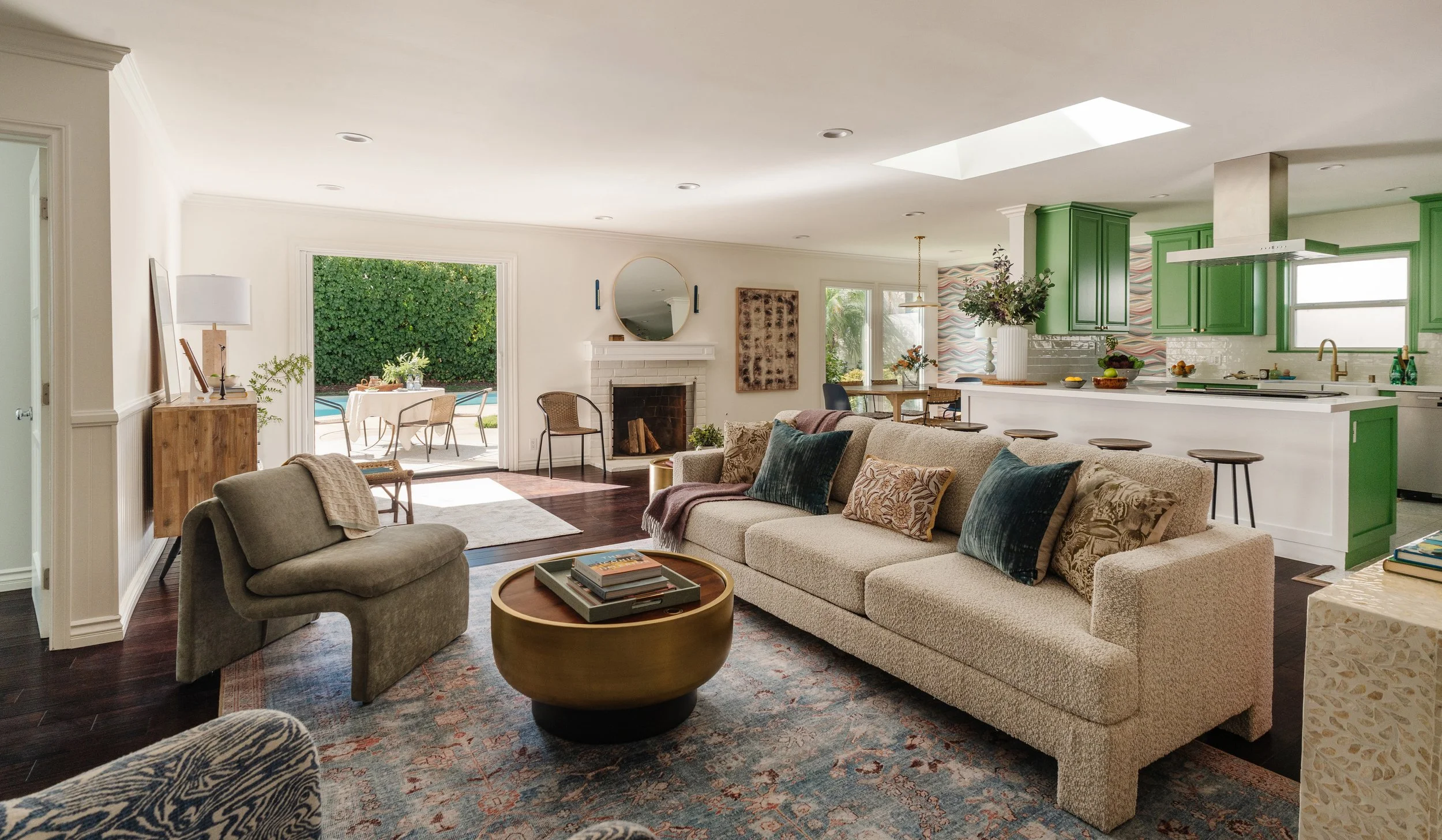 Spacious open-concept living room and kitchen with white walls, dark hardwood floors, beige sofa, green kitchen cabinets, and sliding glass door leading to backyard with patio furniture