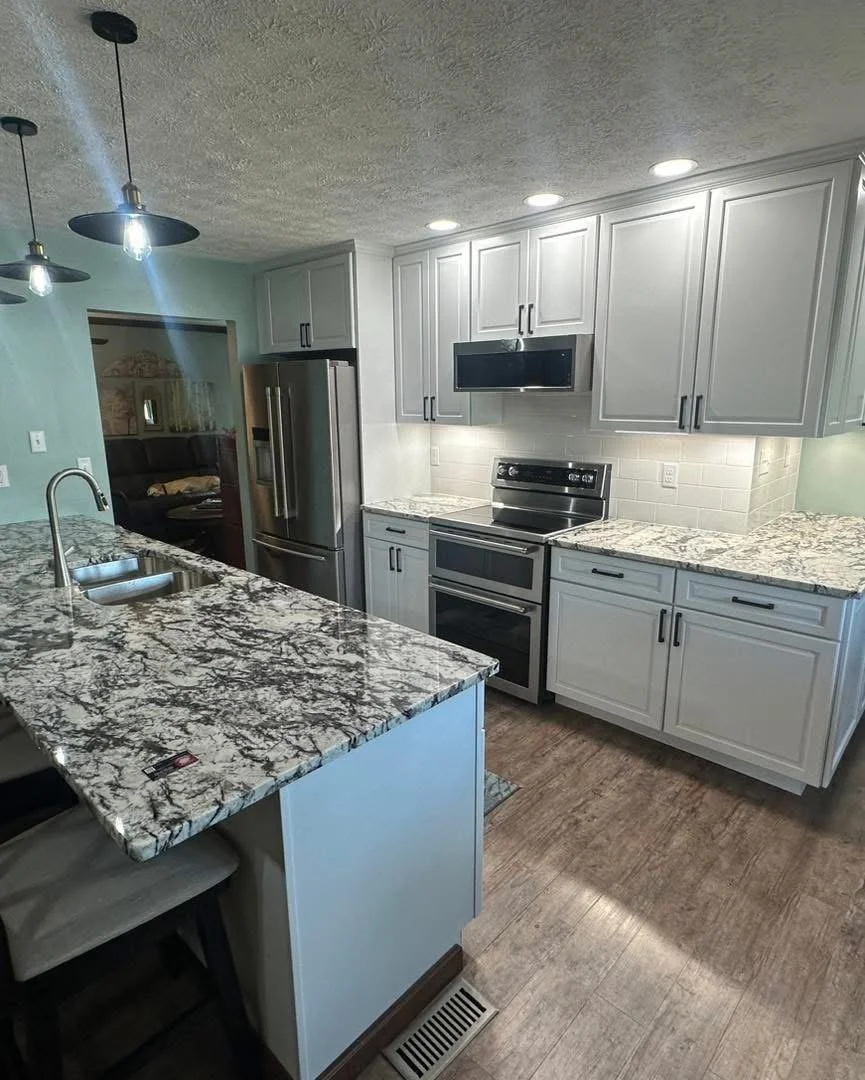 Modern kitchen with white cabinets, stainless steel refrigerator, oven, microwave, granite countertops, and a kitchen island with a sink.