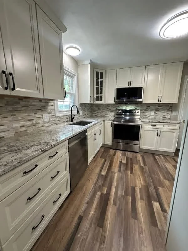 Modern kitchen with white cabinets, granite countertops, tiled backsplash, stainless steel appliances including a stove and dishwasher, and wood flooring.
