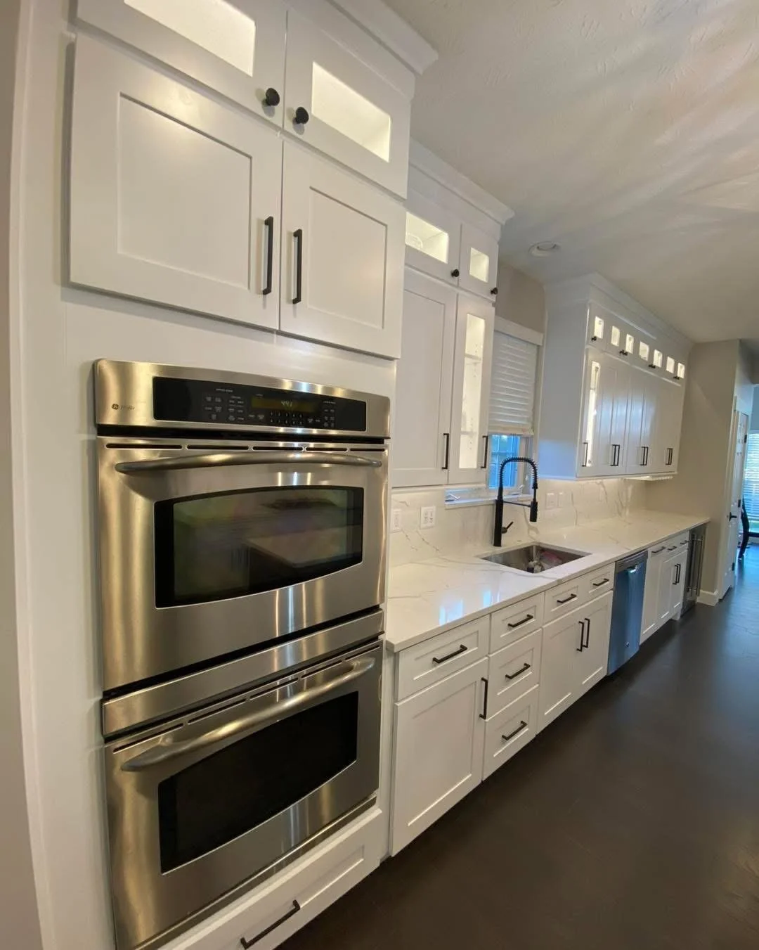 Modern kitchen with white cabinets, stainless steel double oven, marble countertops, and a black faucet over a sink.
