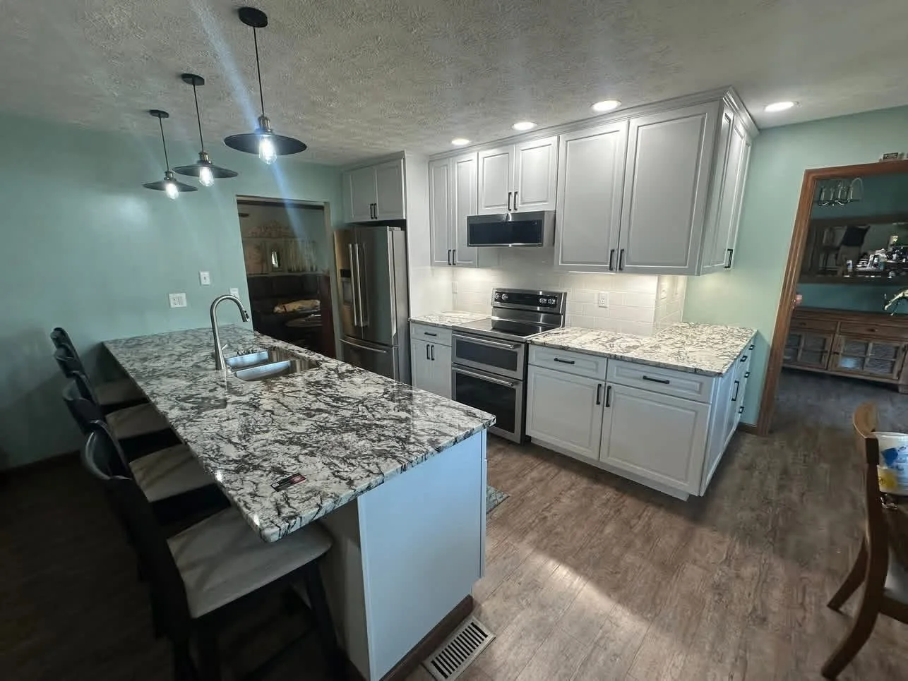 Modern kitchen with white cabinetry, granite countertops, stainless steel appliances, and pendant lighting over the island.