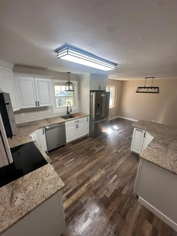 Modern kitchen with white cabinets, granite countertops, hardwood flooring, stainless steel appliances, and ample natural light from two windows.