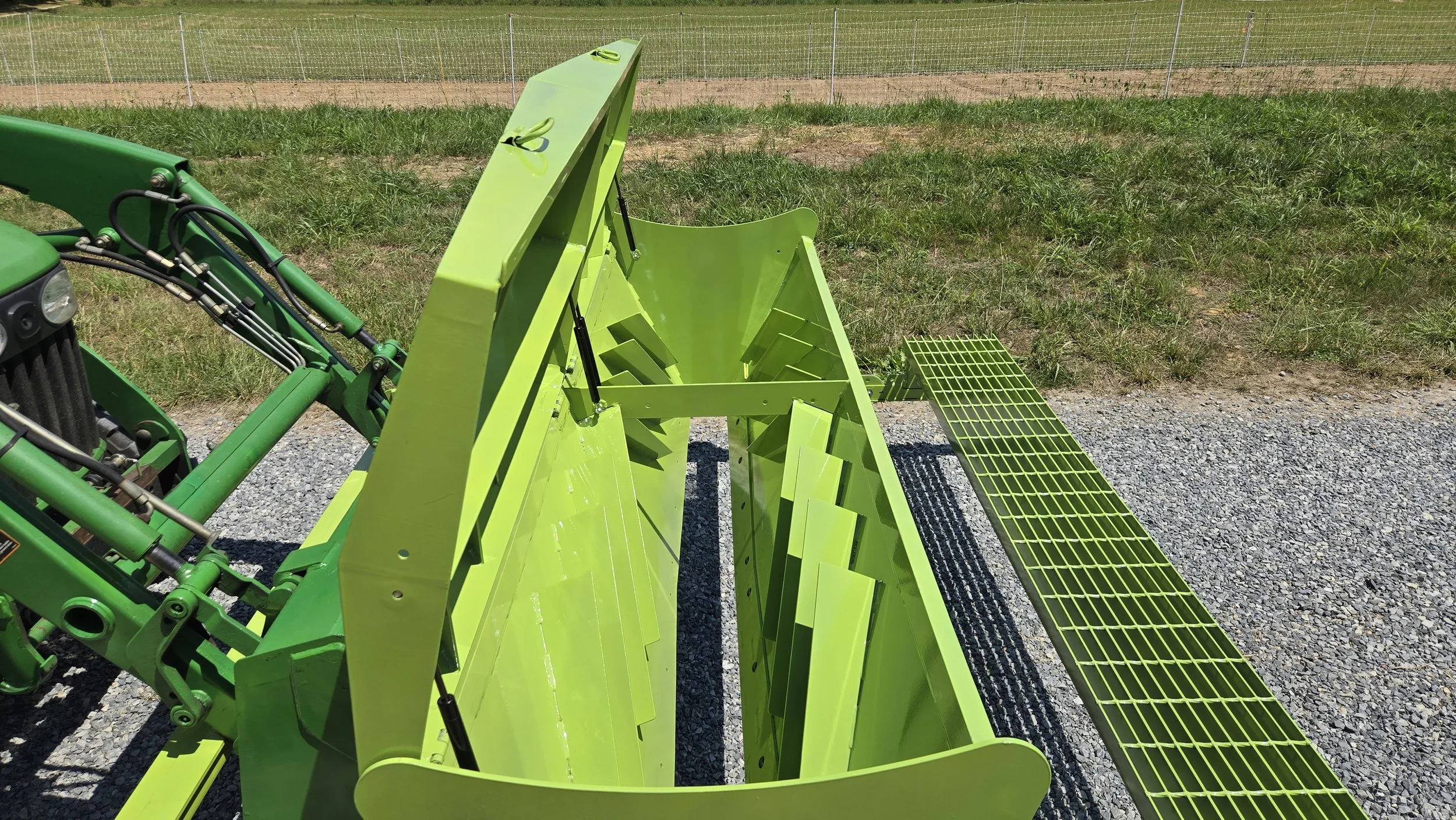 Bright green agricultural machine outdoors on gravel ground with a grassy field and a chain-link fence in the background.