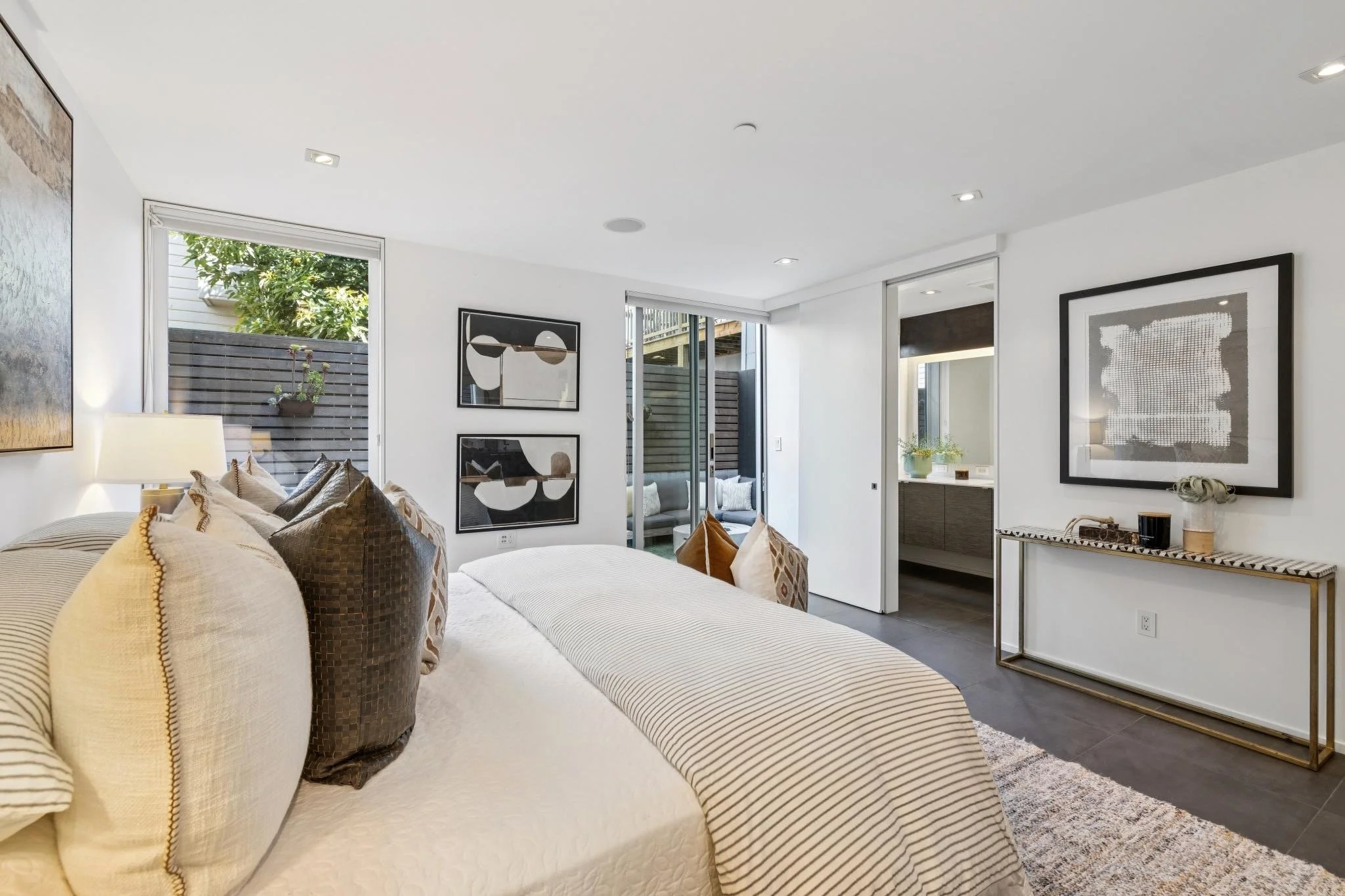 Modern living room with white walls, artwork, large windows, seating area with pillows, and decorative items.