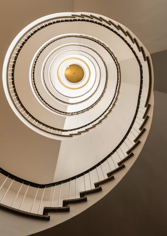 Looking up a spiral staircase from below, with white railings and steps, leading to a yellowish light at the top.