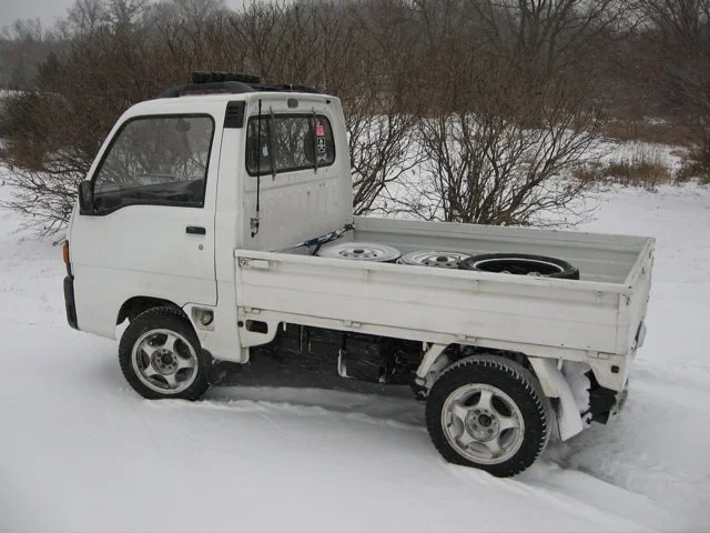 A 1990 Subaru Sambar in the snow with tires and wheels in its bed.