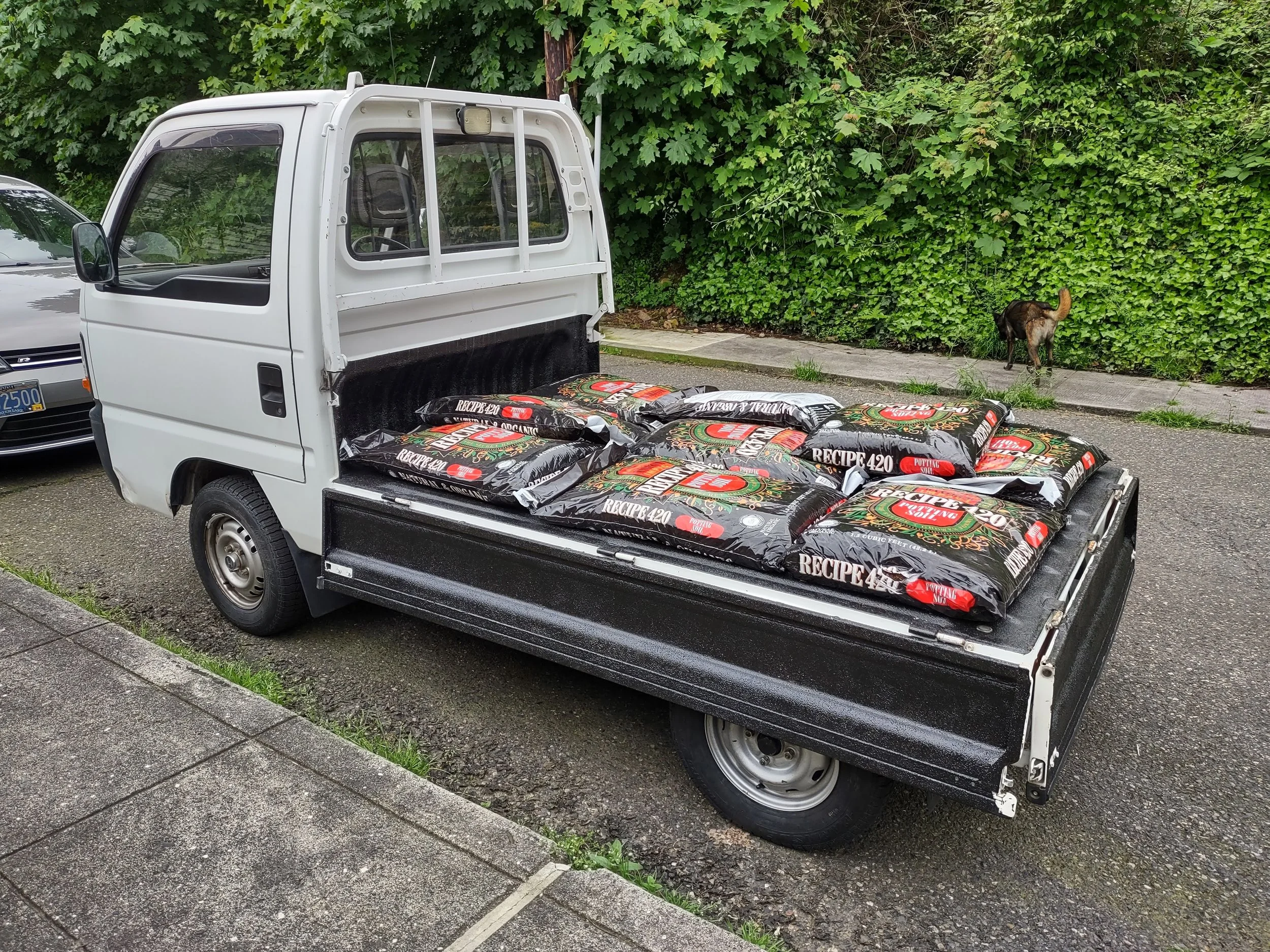 1994 Honda Acty with its bed walls folded down to become a flatbed carrying bags of potting soil.