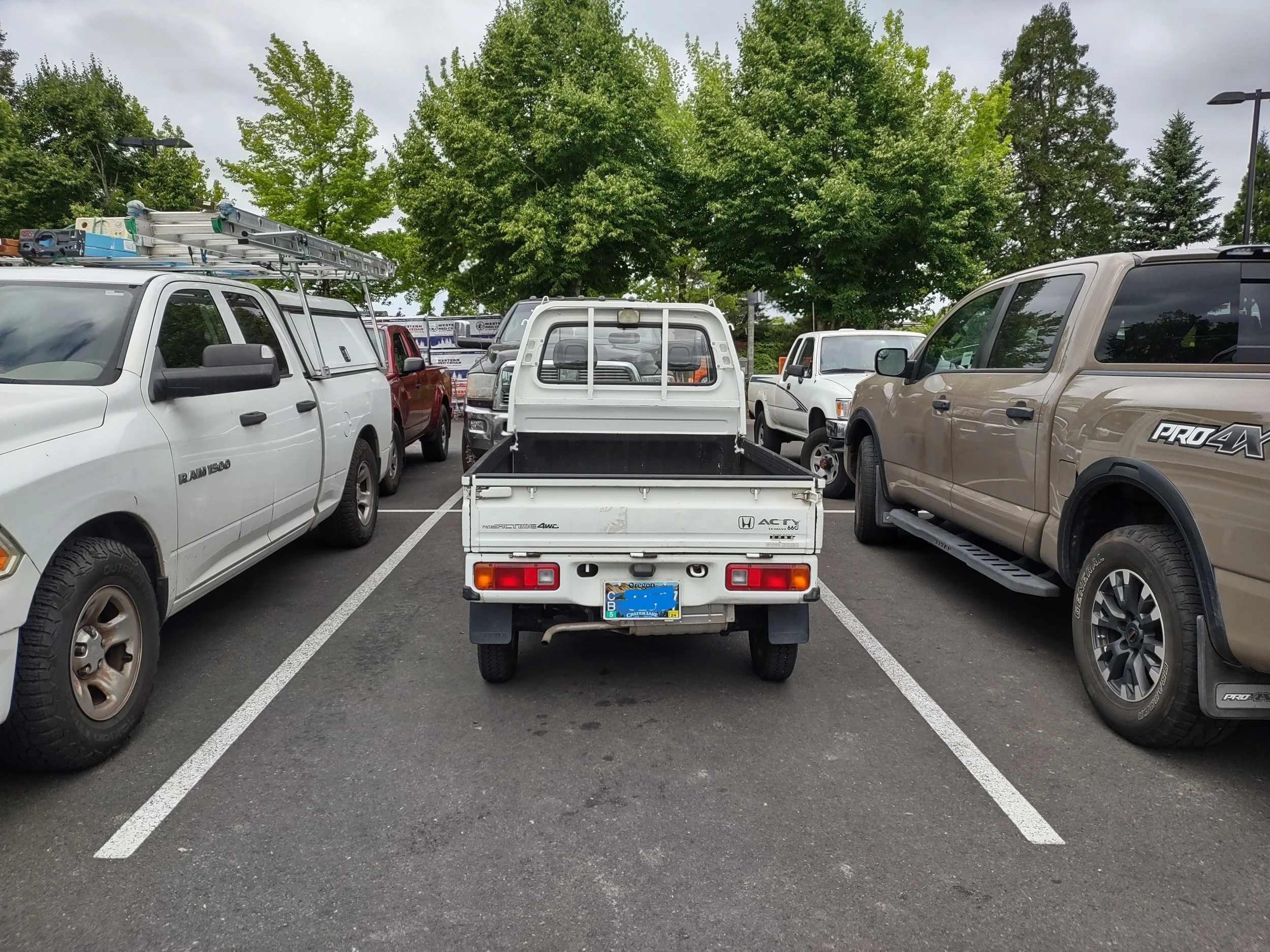 A 1994 Honda Acty parked between two full size pickups.