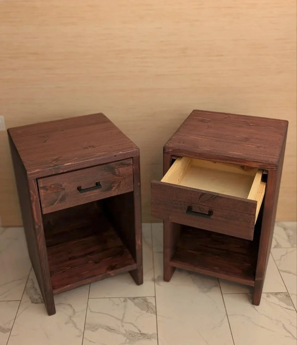 Two wooden nightstands, one with a closed drawer and one with an open drawer, placed on a tiled floor against a light-colored wall.