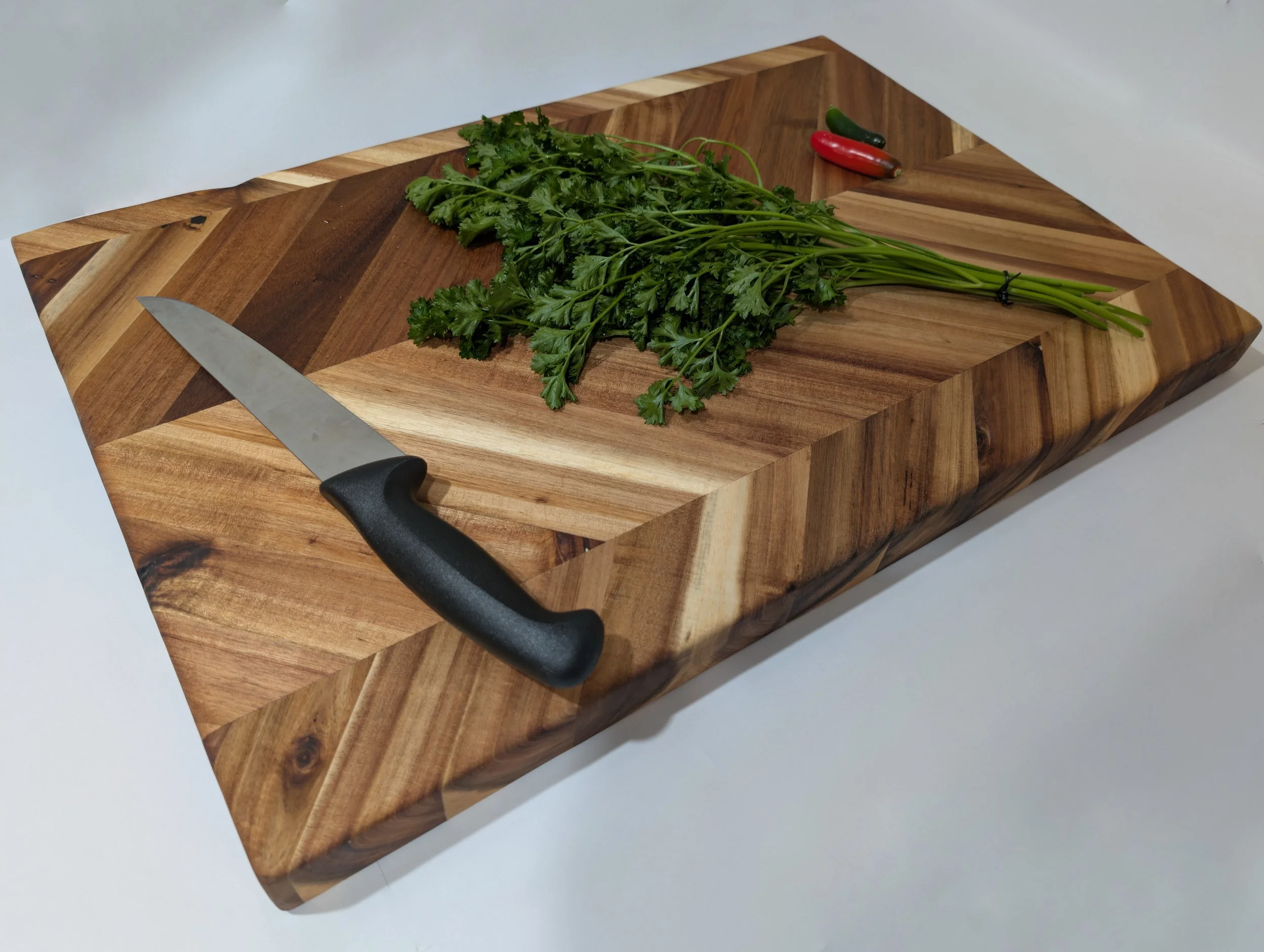 Fresh cilantro bunch with green stems tied together, placed on a wooden cutting board next to a kitchen knife and three small chili peppers, on a white surface.