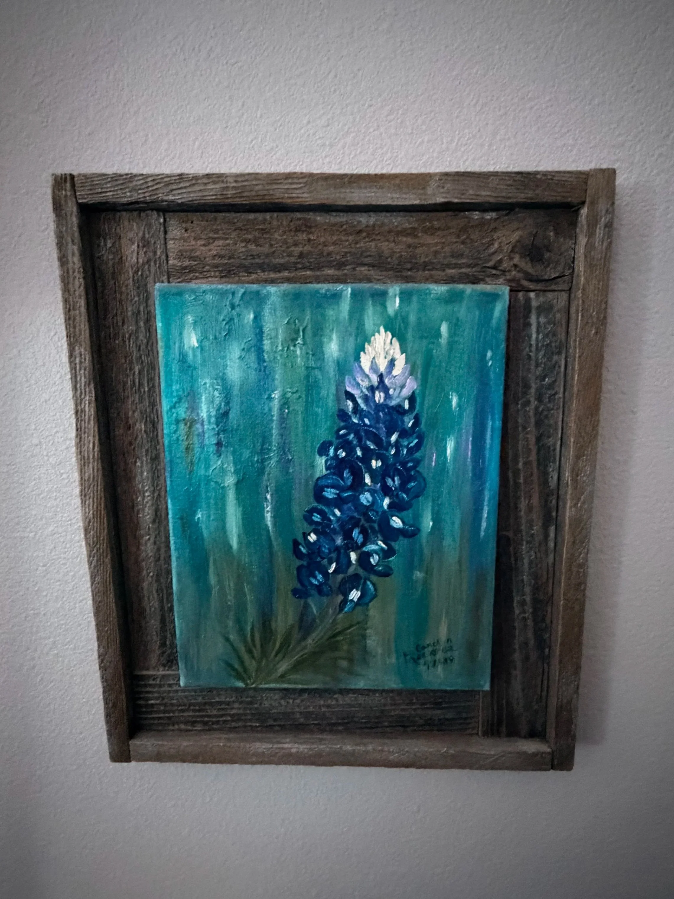 Painting of a blue flowering plant framed in rustic wood, hanging on a wall.
