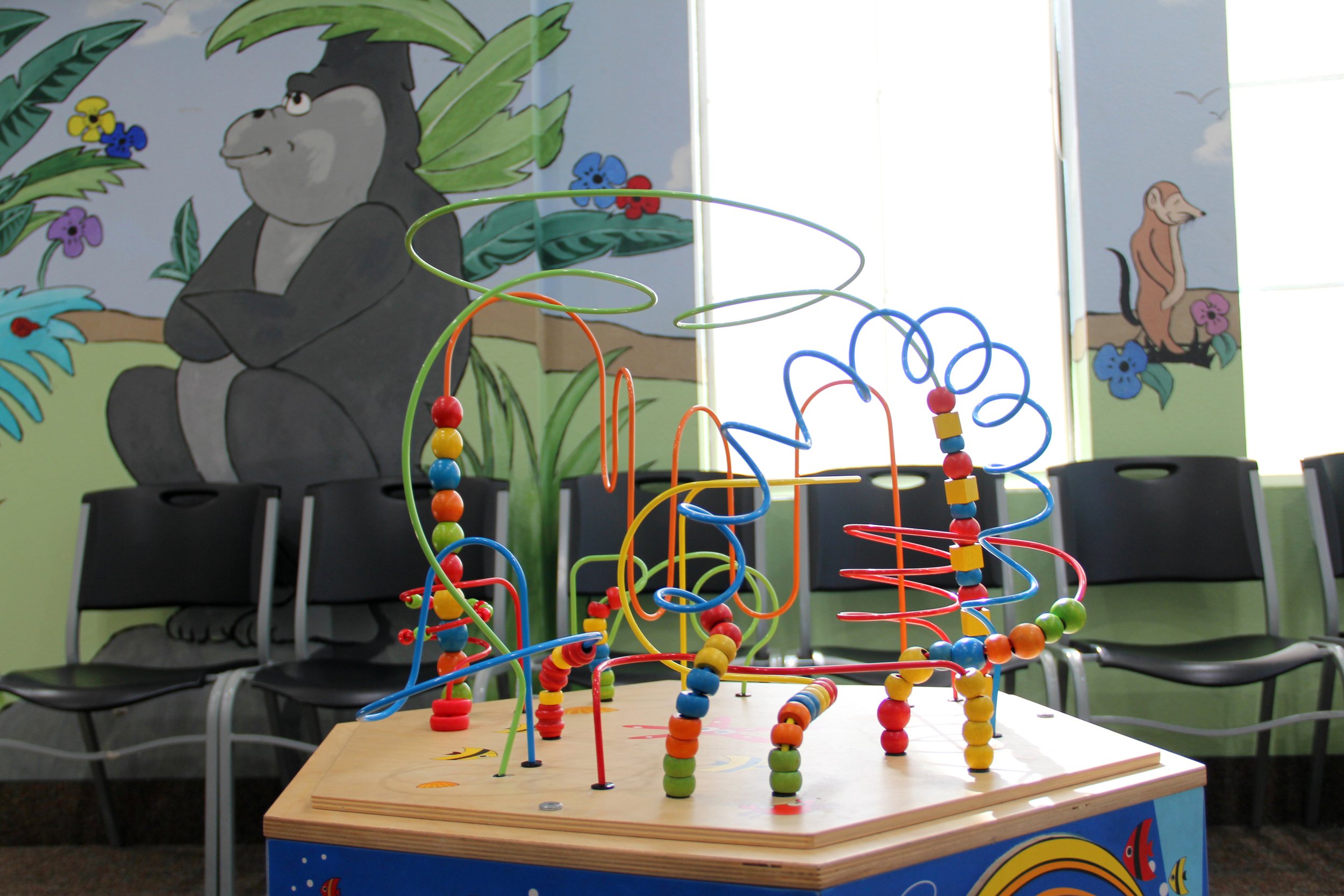 Colorful toy on a wooden table in a room with cartoon animal murals on the walls at Carrollton Pediatrics.