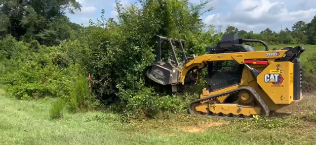 A yellow CAT bulldozer pushing trees and bushes in a grassy area.