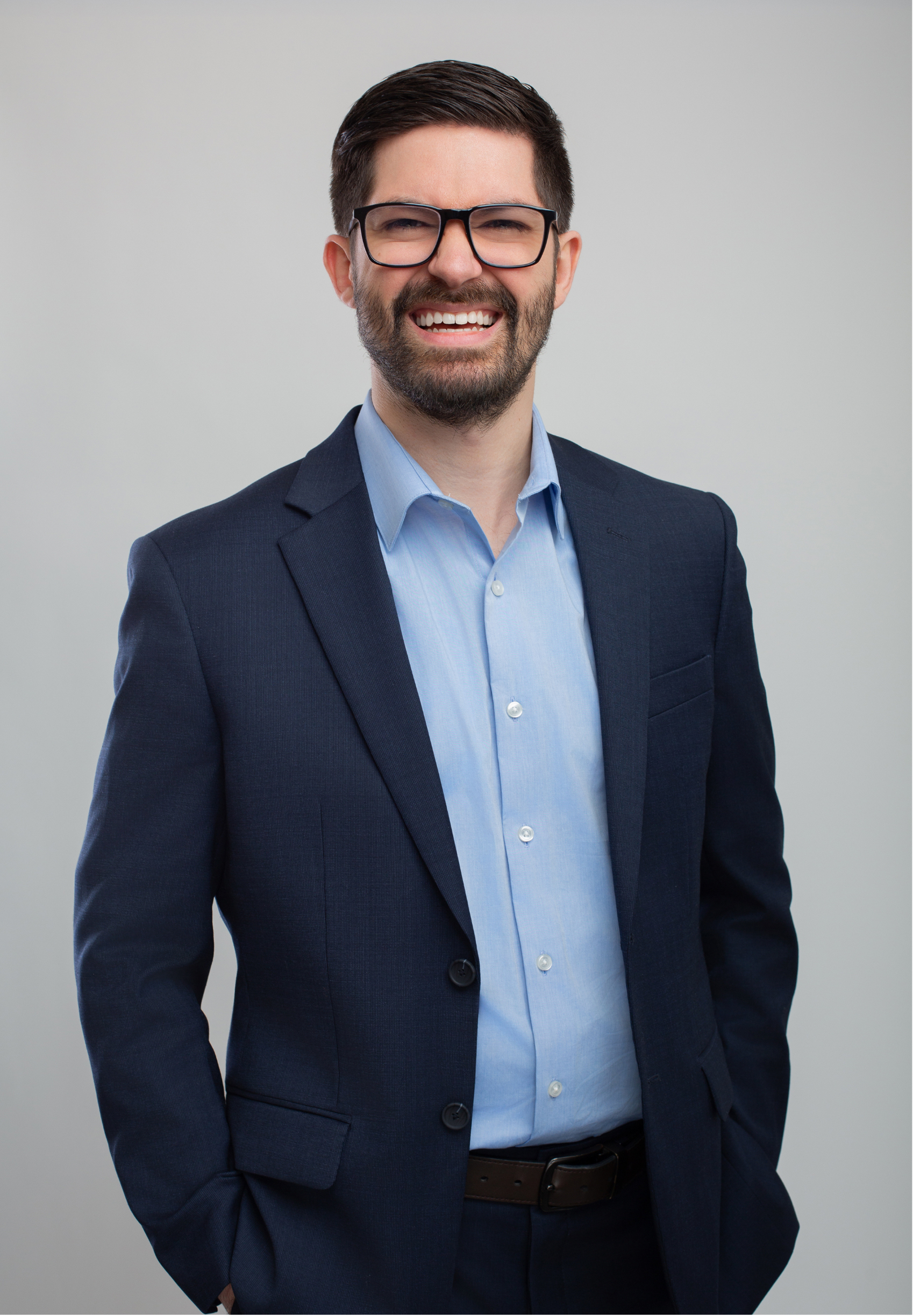 Dr. Joe Rustum, licensed clinical psychologist and executive coach in Nashville, TN, smiling with dark hair and glasses wearing a dark blue suit and light blue shirt posed against a gray background.