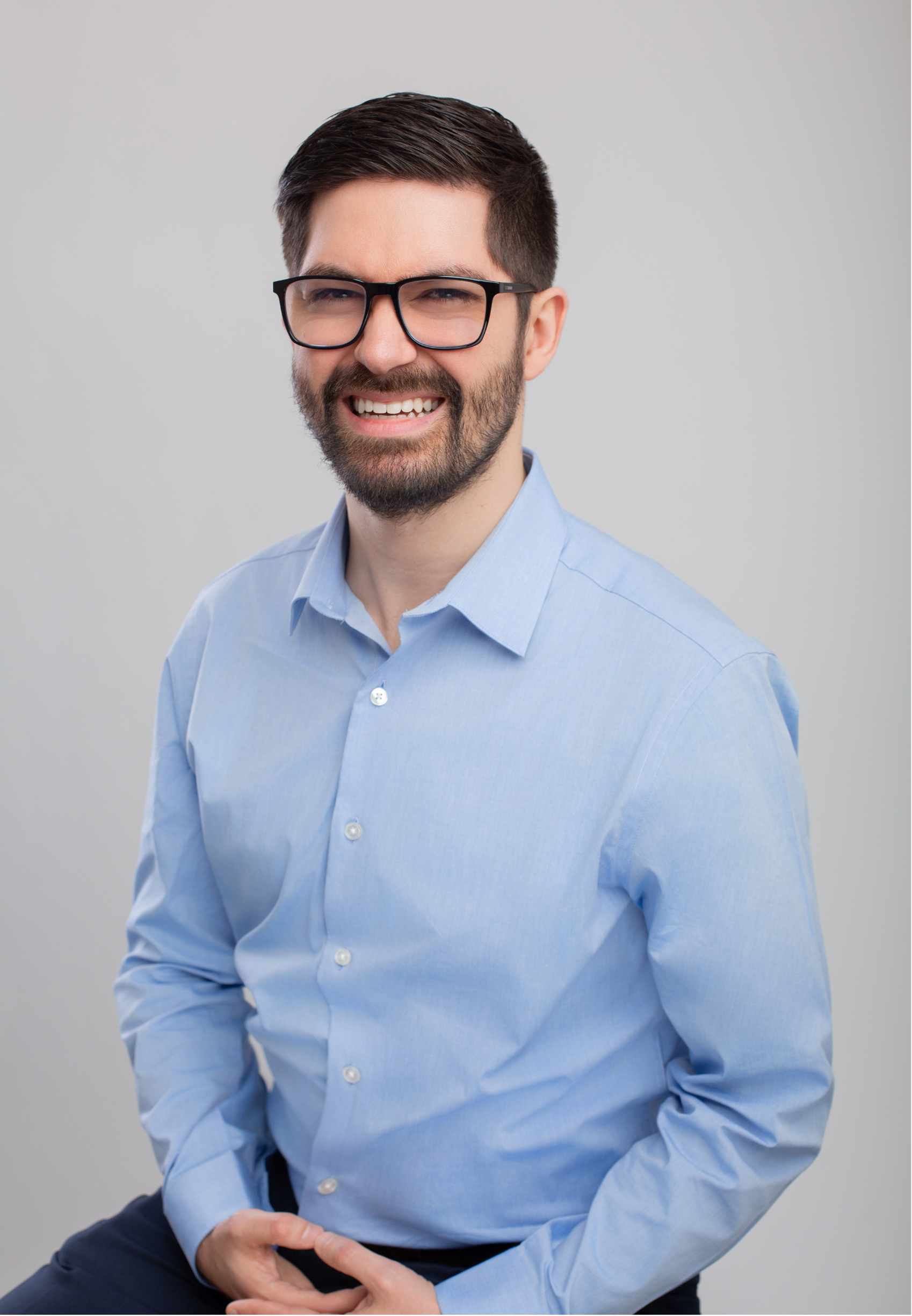 Dr. Joe Rustum, licensed clinical psychologist and executive coach in Nashville, TN, with dark hair, glasses, and a beard smiling, wearing a light blue dress shirt against a plain background.