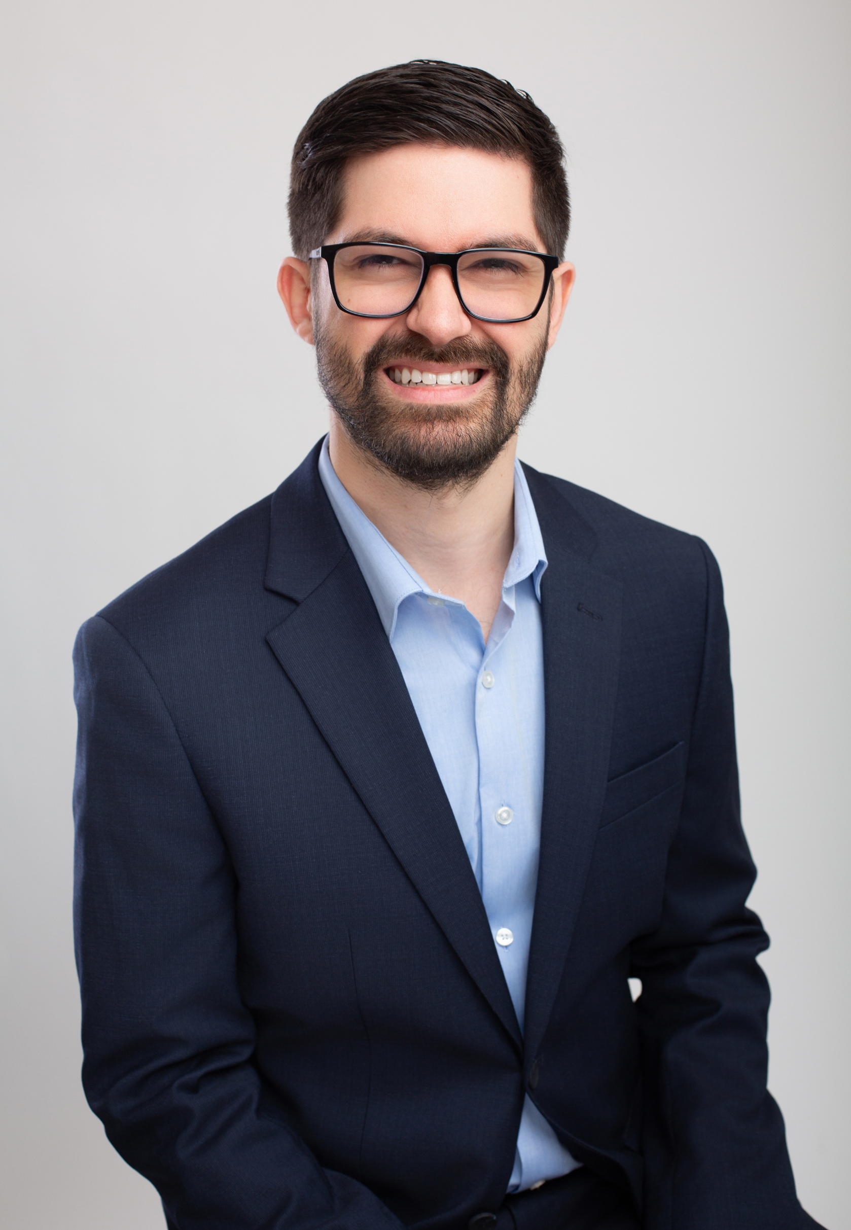 Dr. Joe Rustum, licensed clinical psychologist and executive coach in Nashville, TN, in a dark blue suit with glasses, smiling, against a light gray background.