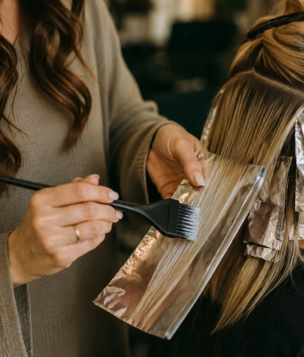 A hairdresser applying hair color to a client's hair using a brush and foil in a salon.