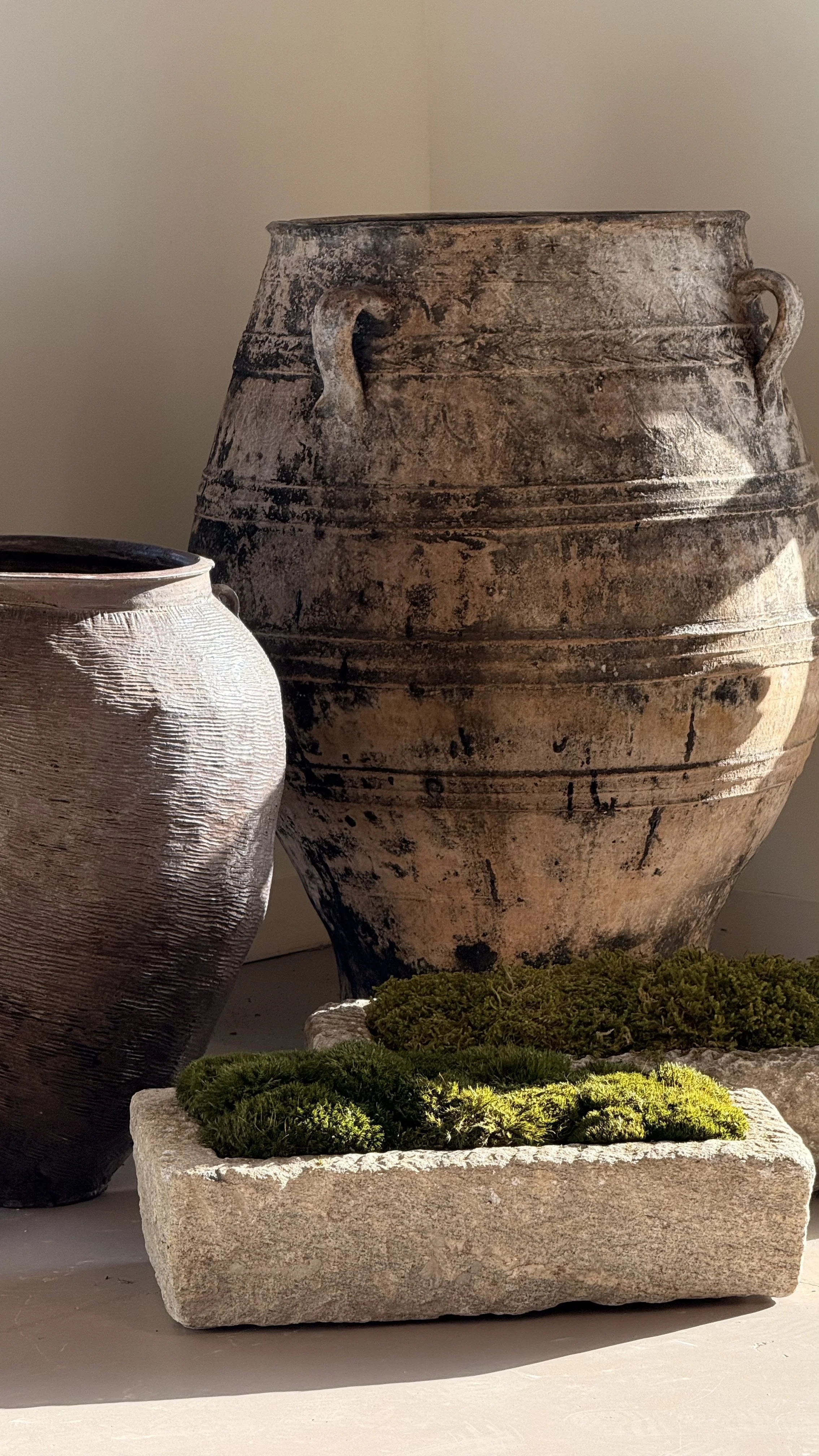 Close-up of weathered ceramic urns and a rectangular stone planter filled with moss.