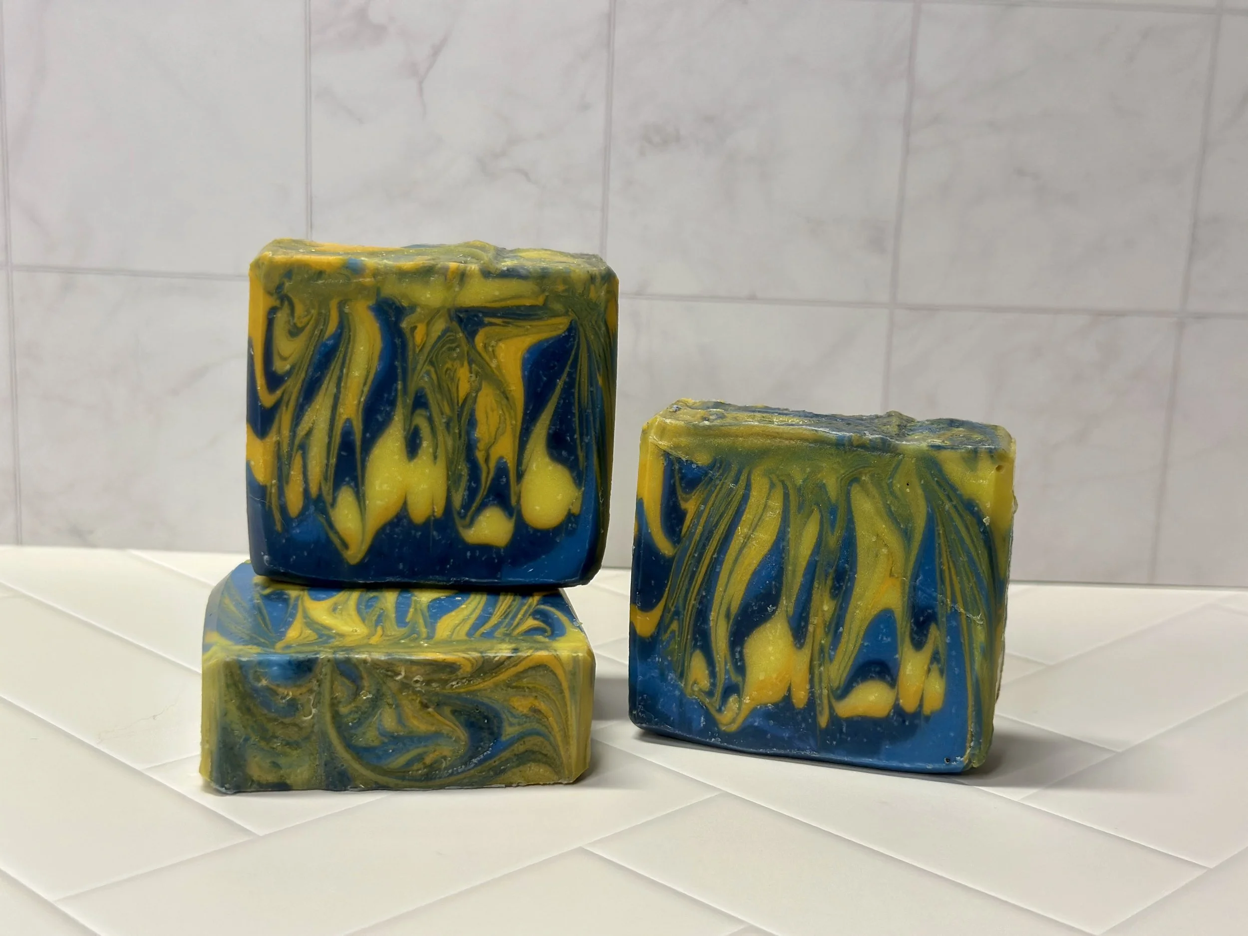 Photo of handcrafted artisan soaps, posed to appeal. The soaps are made of deep blue and bright yellow swirls.