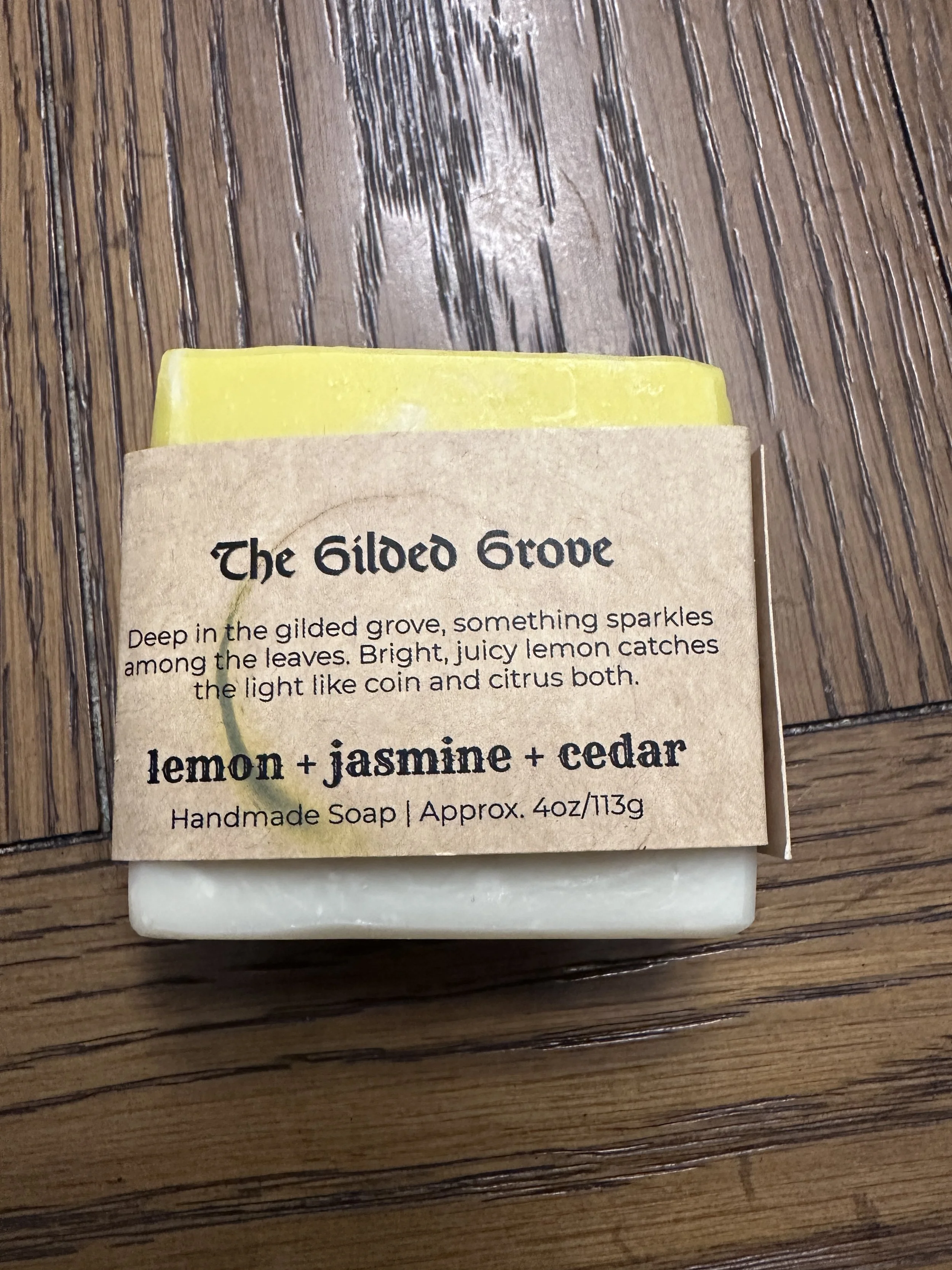 Photo of a handcrafted soap that's about half lemon yellow and half natural off-white. Includes a label with the soap's name -- The Gilded Grove.