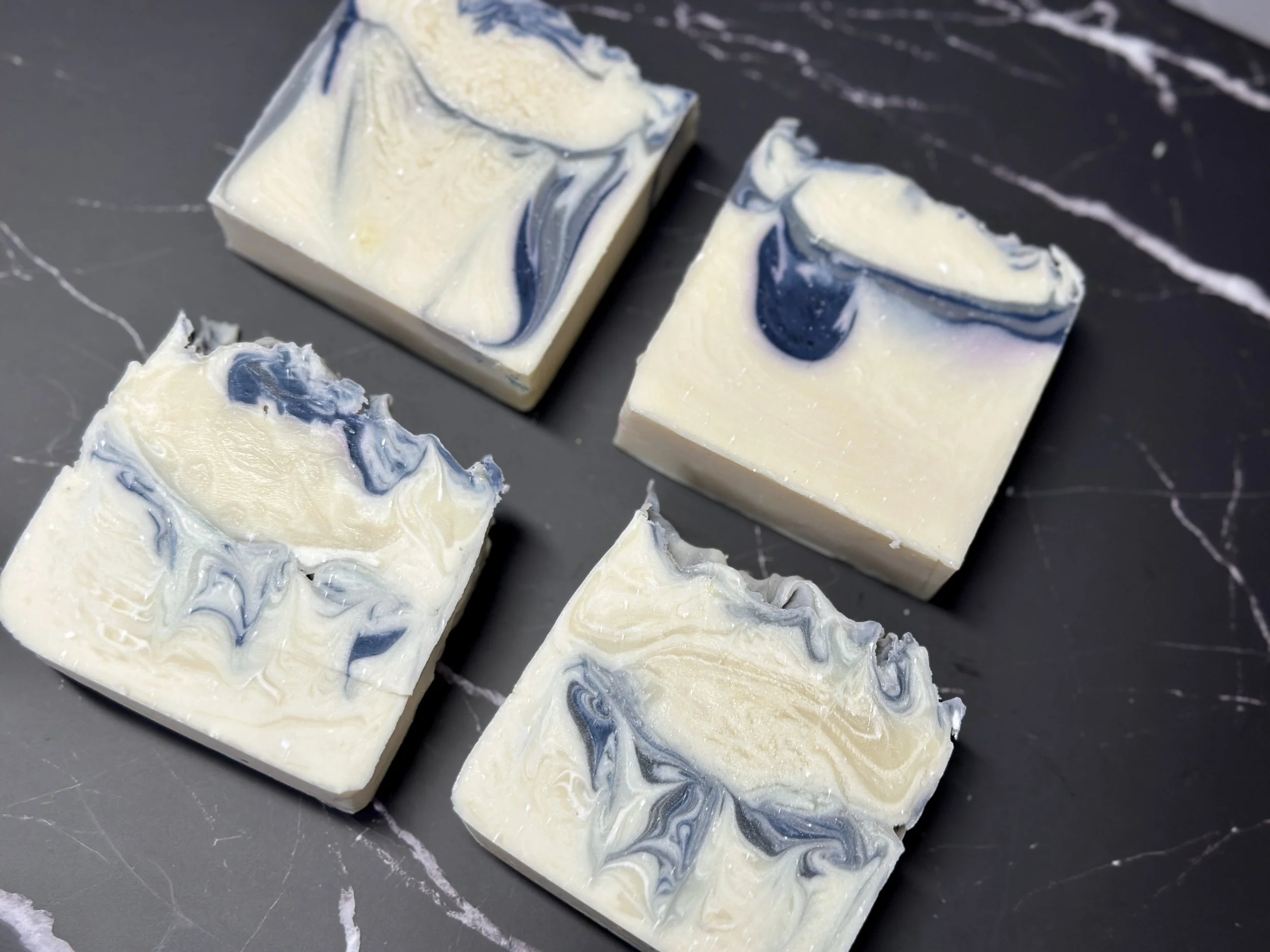 Photo of handcrafted artisan soaps, posed to appeal. The soaps are primarily a bright, icy white with threads of deep blue and a tinge of lilac.